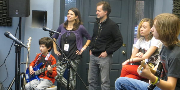 Tory and Vanessa Ridder stand behind their son Wolfe, 9, while watching students in the School of Rock’s performance program practice at their weekly band rehearsal. Photo by Danielle Brody