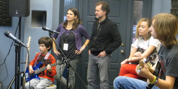 Tory and Vanessa Ridder stand behind their son Wolfe, 9, while watching students in the School of Rock”™s performance program practice at their weekly band rehearsal. Photo by Danielle Brody