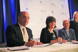 WMC President and CEO Michael D. Israel and Dr. Mary P. Leahy, CEO of Bon Secours Charity Health System, sign the joint agreement at Good Samaritan Hospital in Suffern. In background is WMC board Chairman Mark Tulis. Photo by John Golden